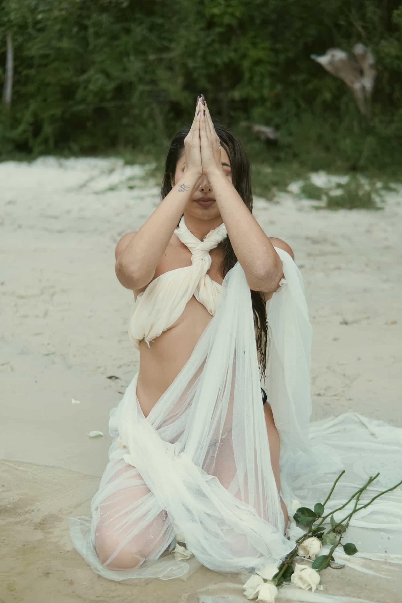 Sahara Rose kneeling in prayer on the sand with white roses